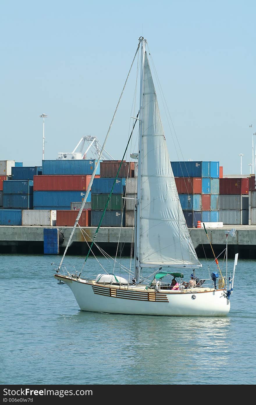 Sailboat sailing at port in front of cargo containers