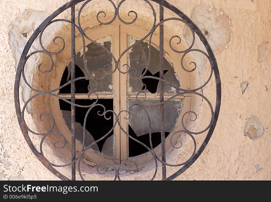 Old smashed circlular window with iron grate covering. Old smashed circlular window with iron grate covering