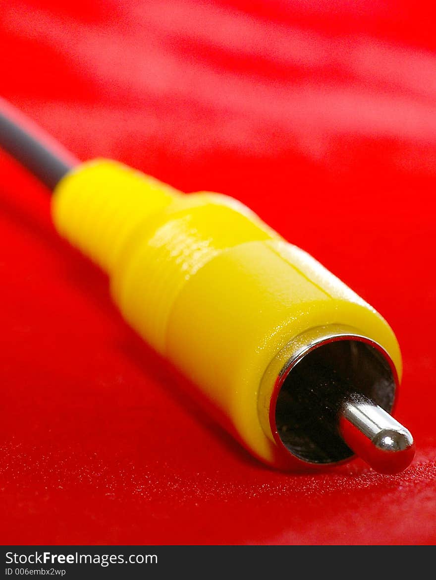 Closeup of an RCA-style (yellow) video cable against a bright red background. Closeup of an RCA-style (yellow) video cable against a bright red background