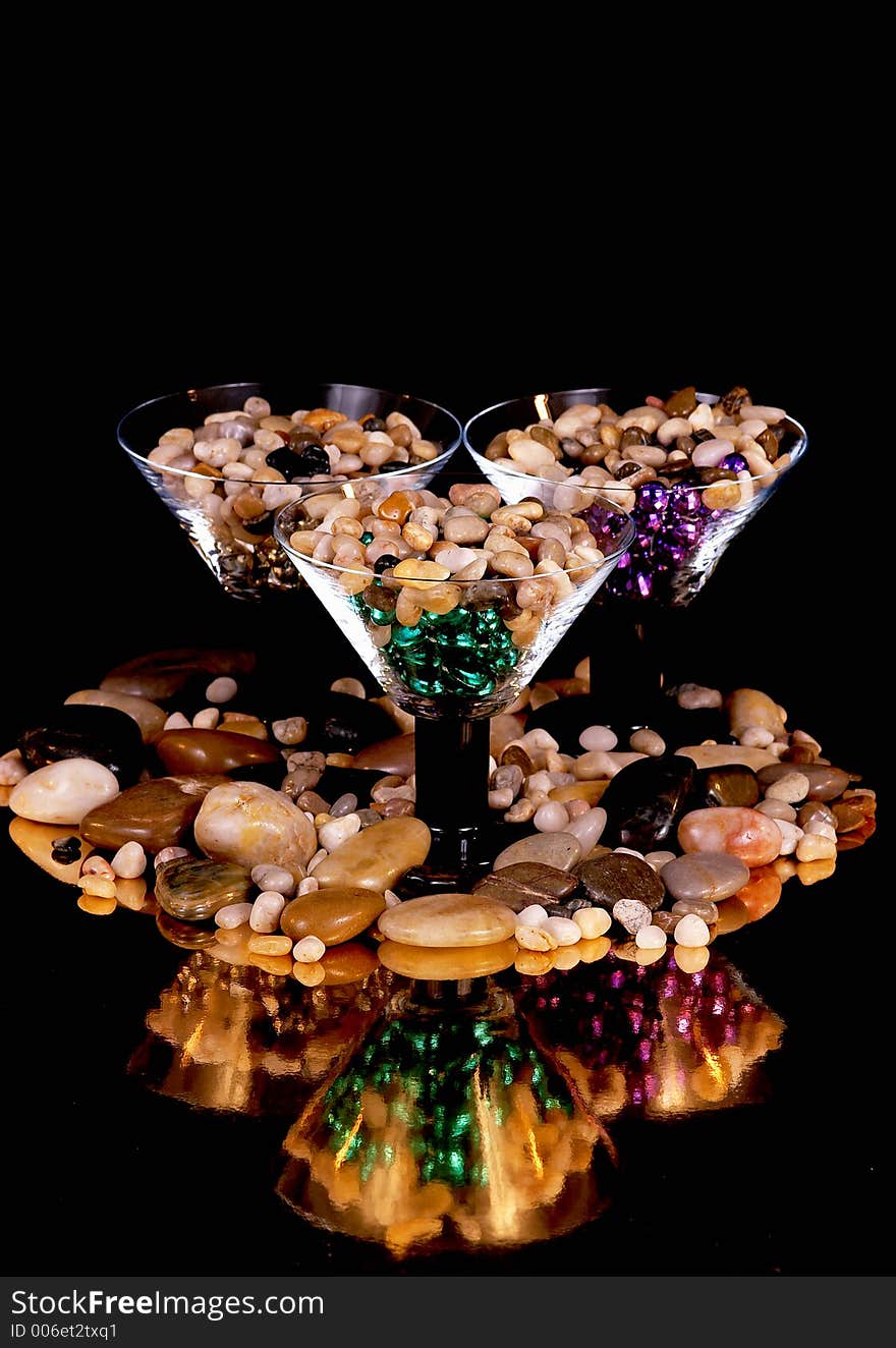 3 martinin glasses with colorful beads and stones reflected off a gold base on a black background. 3 martinin glasses with colorful beads and stones reflected off a gold base on a black background