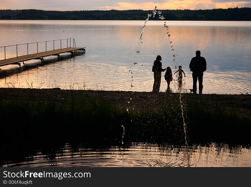 A lake in denmark , a so called bath bridge on a danish lake A family on the beach at the sunset