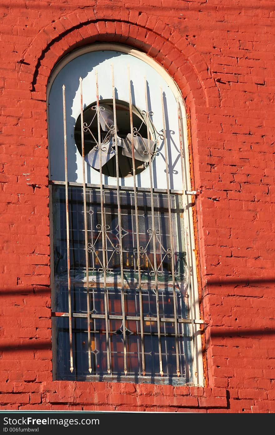 Old brick building's window with iron bars. old electric fan cools the old rooms.