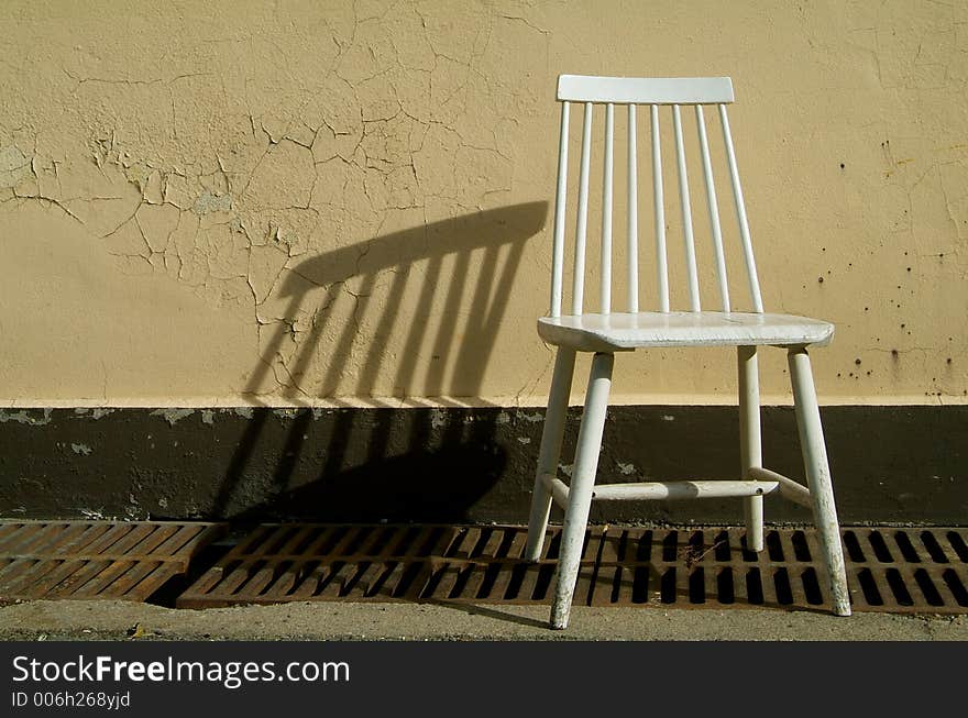 White, wooden chair throwing a shadow on a yellow wall. White, wooden chair throwing a shadow on a yellow wall