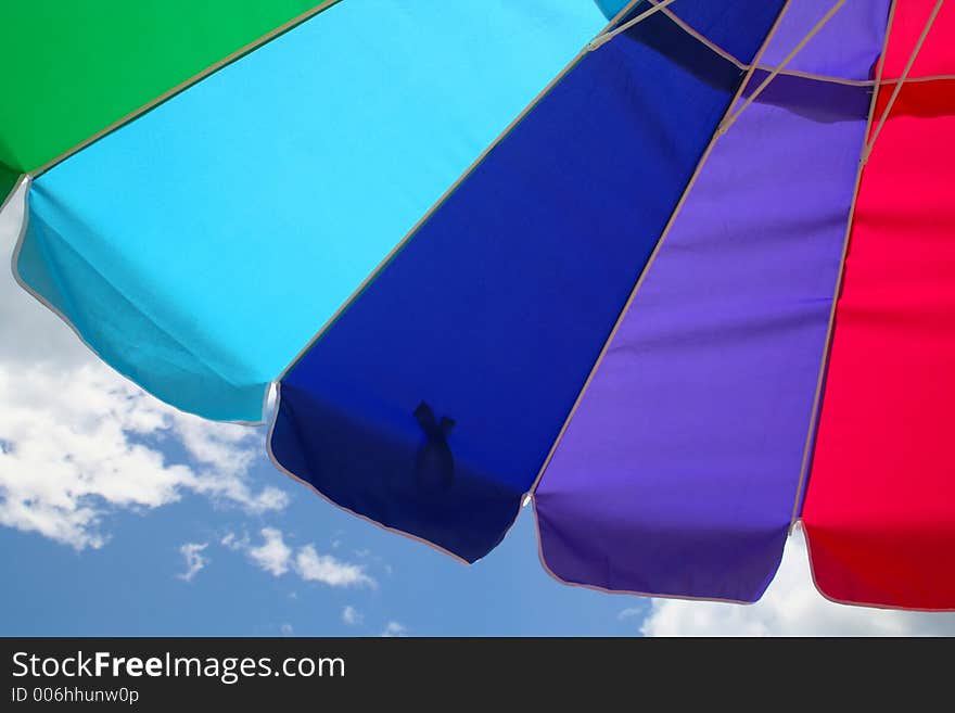 The Colorful Arc of a Beach Umbrella is Displayed against a Background of Blue Sky and Clouds. The Colorful Arc of a Beach Umbrella is Displayed against a Background of Blue Sky and Clouds.