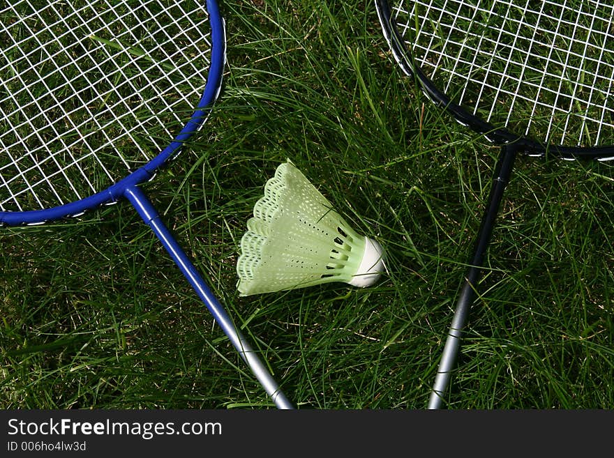 Two badminghton rackets laying in the grass with the ball in the middle. Two badminghton rackets laying in the grass with the ball in the middle