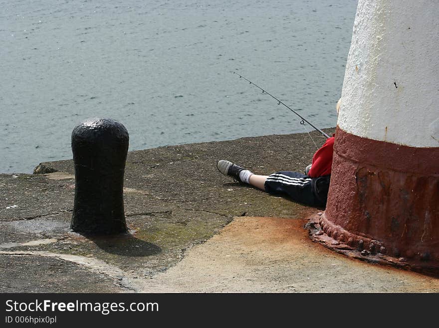 Child leaning againt small lighthouse fishing off the end of a pier. Child leaning againt small lighthouse fishing off the end of a pier