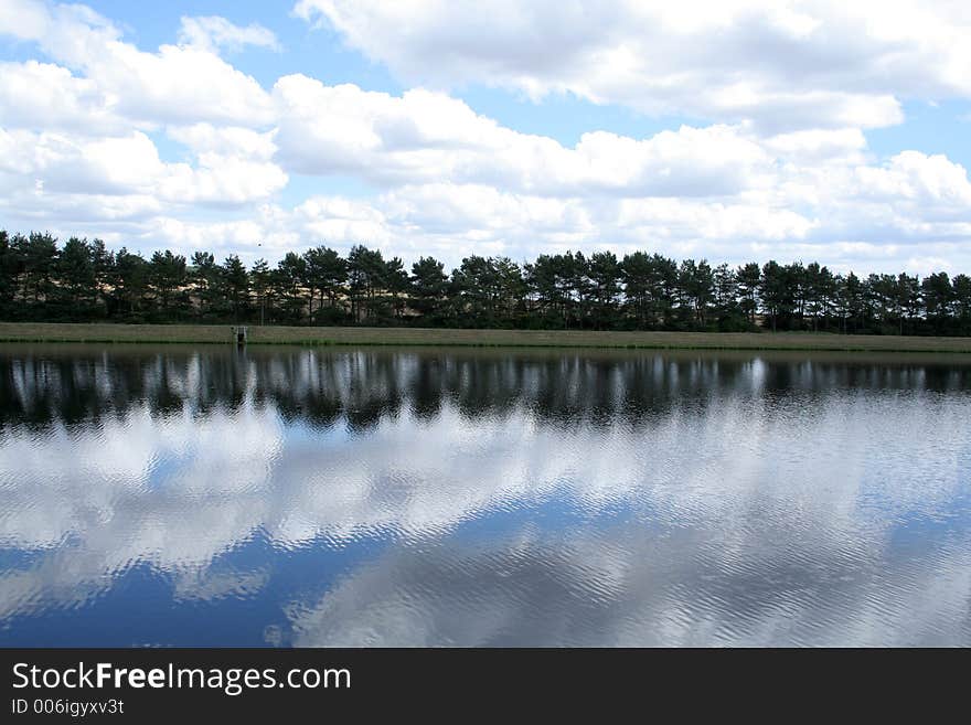 On a beauiful summers day the clouds and trees are reflected in the water to give a mirror image. On a beauiful summers day the clouds and trees are reflected in the water to give a mirror image