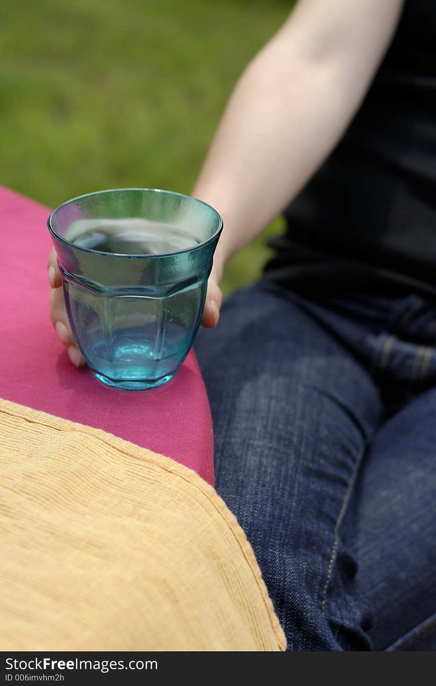 Female hand holding a turquoise glass on purple tablecloth