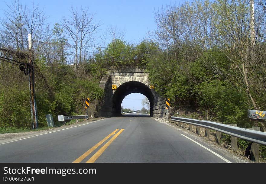 A narrow urban road running under a viaduct.