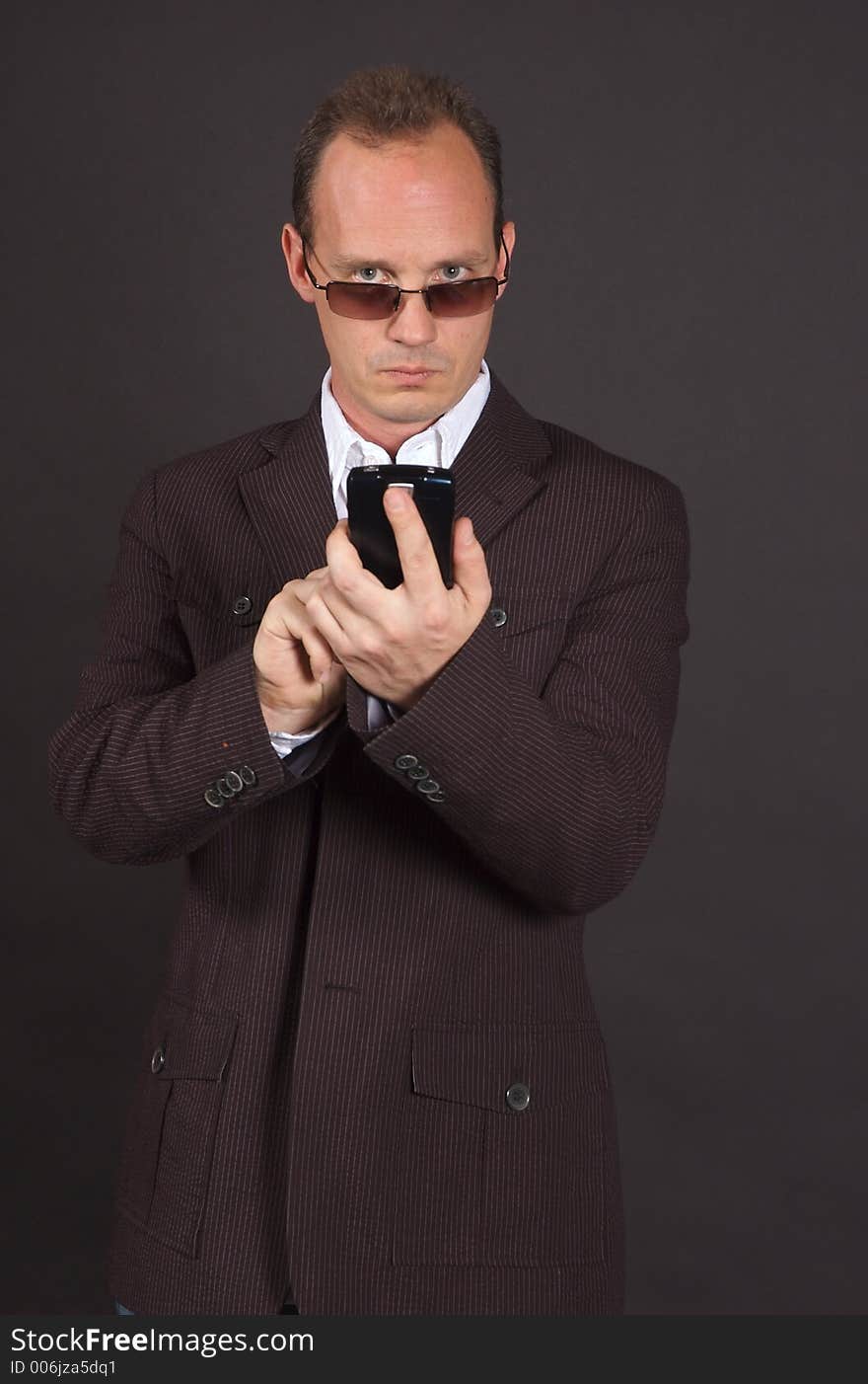 A man in a sportsjacket and sunglasses, punching in information to his mobile device. A man in a sportsjacket and sunglasses, punching in information to his mobile device