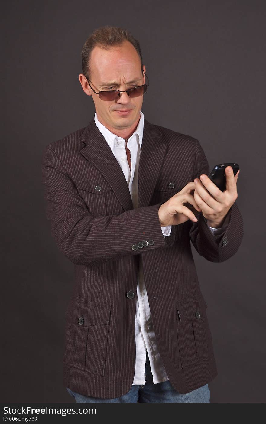 A man in a sportsjacket and sunglasses, punching data into his mobile device. A man in a sportsjacket and sunglasses, punching data into his mobile device