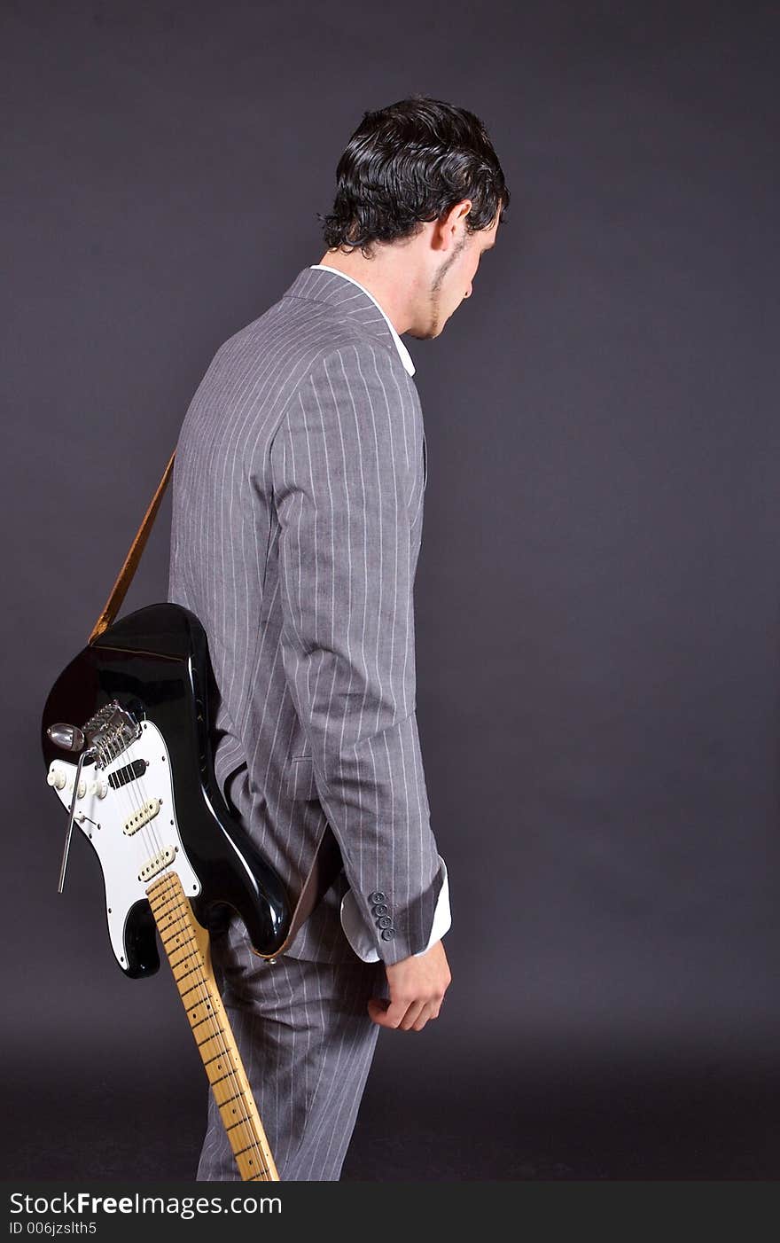 A man in a pinstriped suit with an electric guitar slung over his shoulder