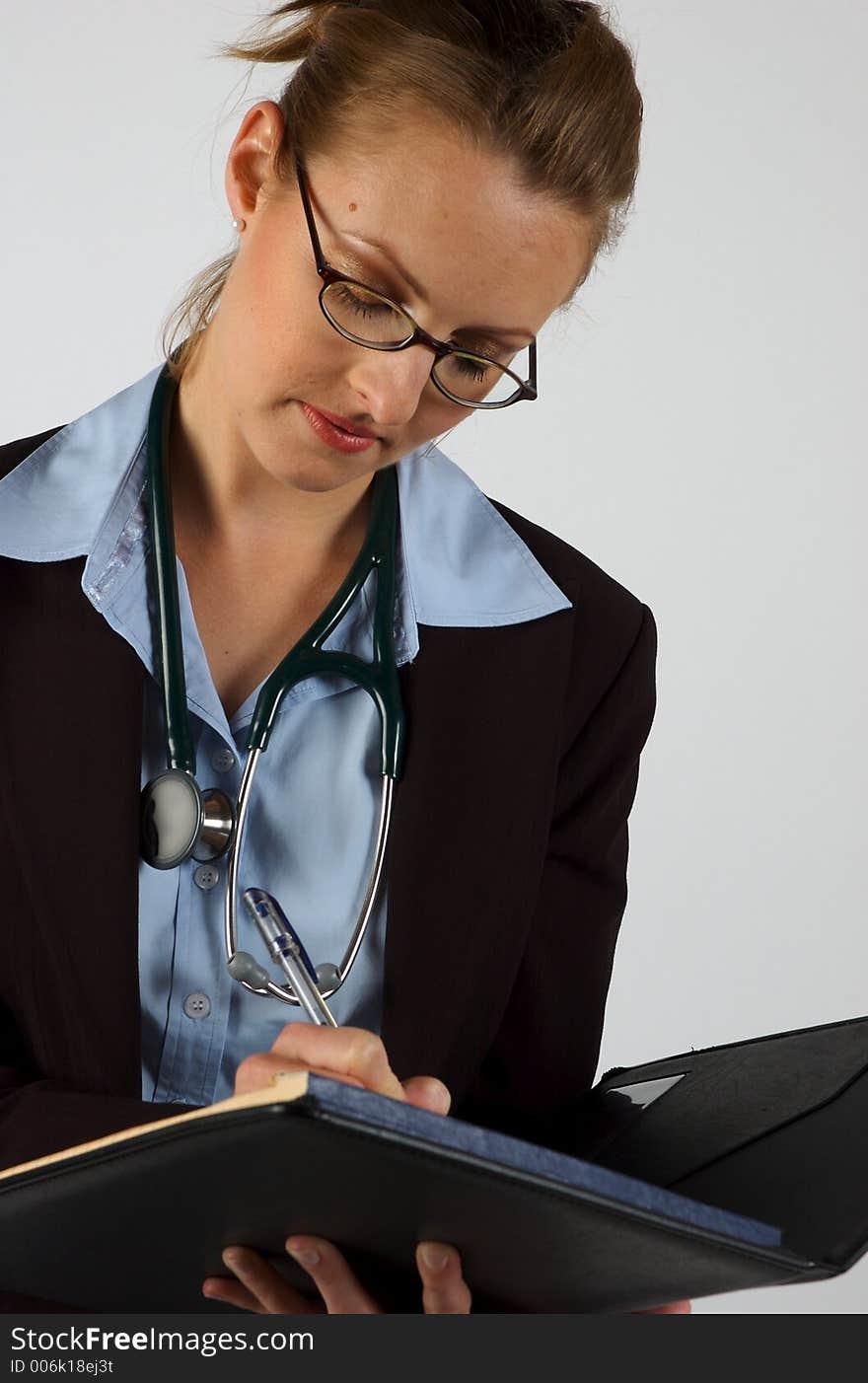 A woman in a business suit with a stethoscope around her neck, writing into a notepad. A woman in a business suit with a stethoscope around her neck, writing into a notepad