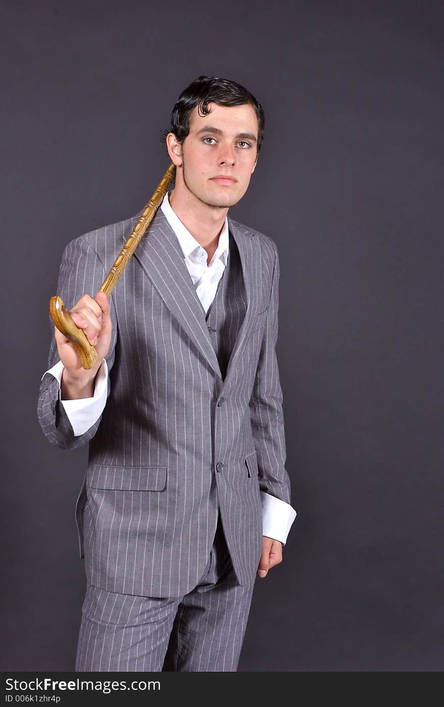 A man in a pinstriped suit holding a cane and looking up towards the camera