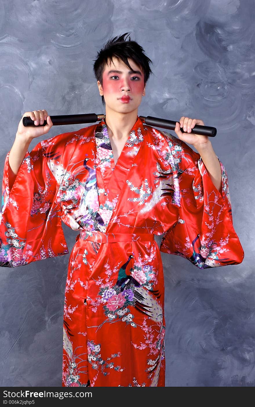 A man in a Geisha outfit, holding a set of Nunchaku. A man in a Geisha outfit, holding a set of Nunchaku