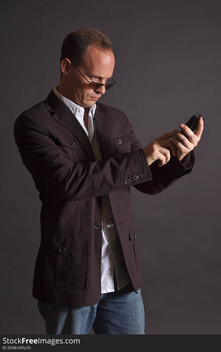 A man in a sportsjacket and sunglasses, punching in information to his mobile device. A man in a sportsjacket and sunglasses, punching in information to his mobile device