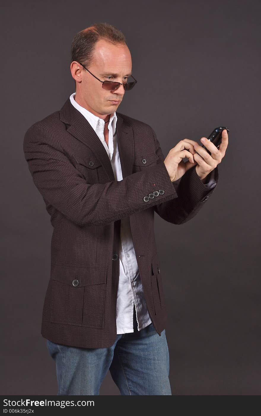 A man in a sportsjacket and sunglasses, punching in information to his mobile device. A man in a sportsjacket and sunglasses, punching in information to his mobile device