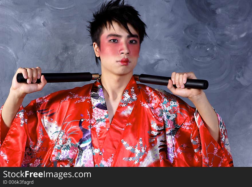 A man in a Geisha outfit, holding a set of Nunchaku. A man in a Geisha outfit, holding a set of Nunchaku