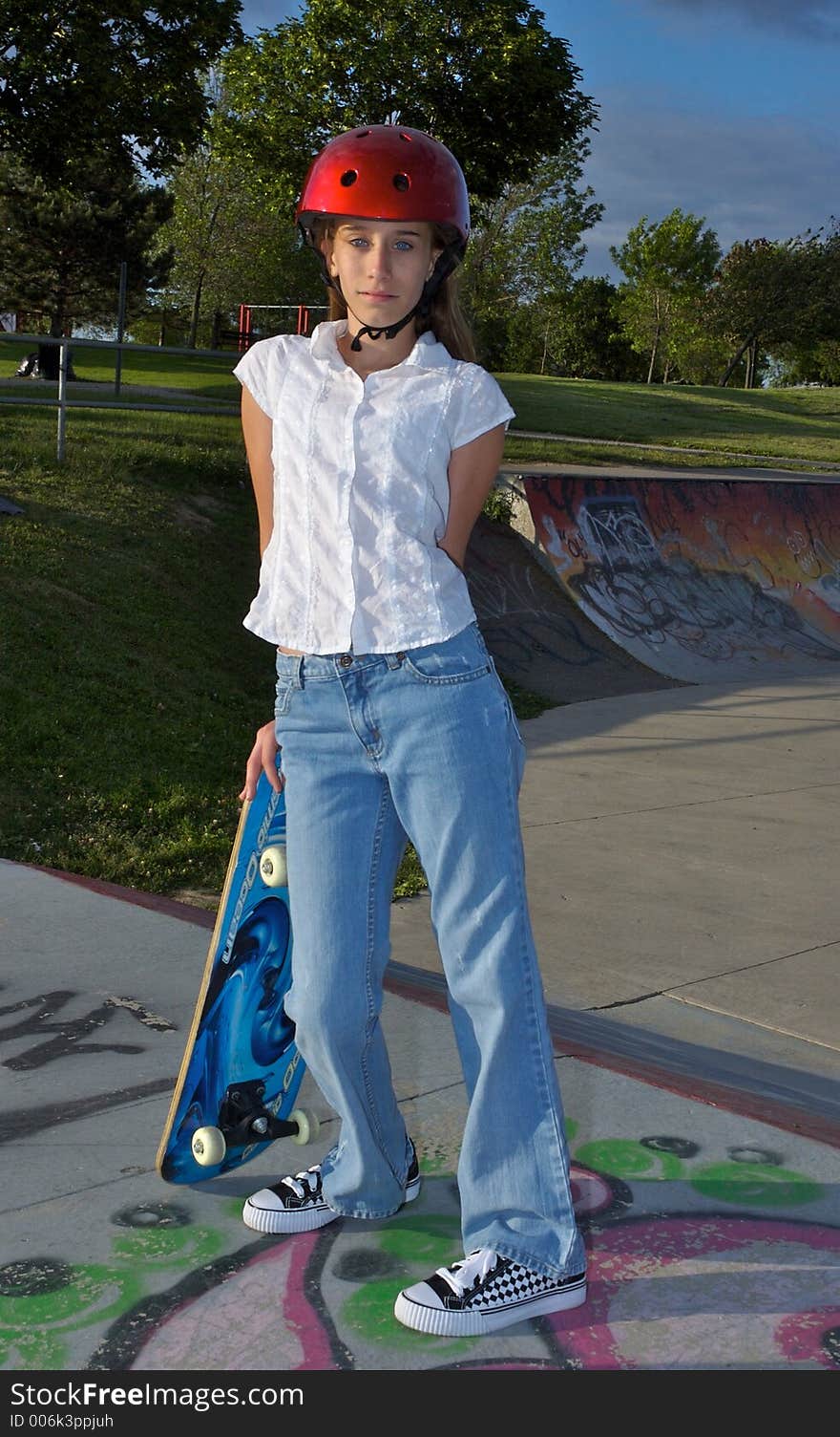 A young girl leaning against her skateboard, wearing a helmet. A young girl leaning against her skateboard, wearing a helmet