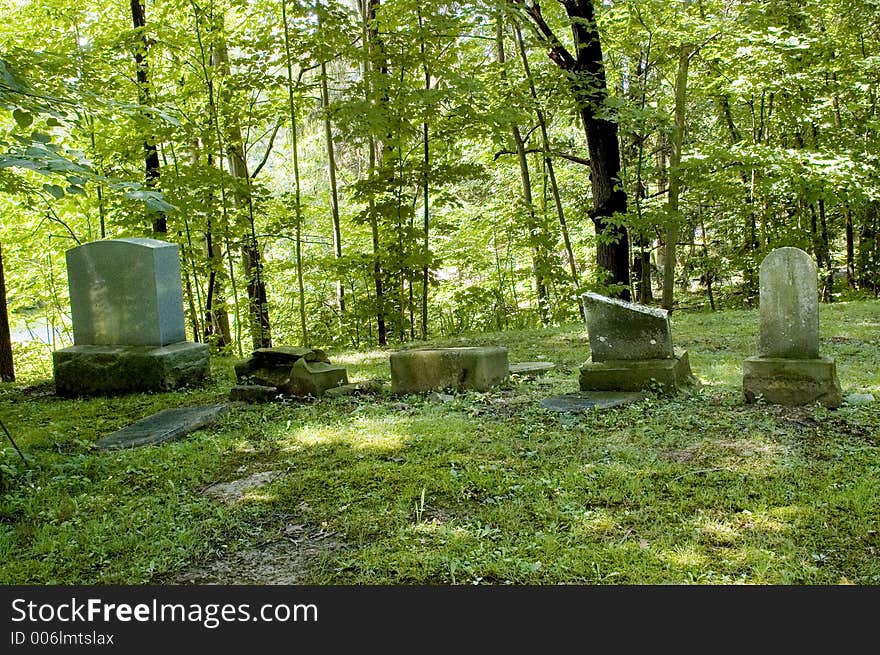 A row of early grave markers in a country cemetery.  Stones are very old, broken and weathered. Contrasted by the new headstone at the far left of the image. A row of early grave markers in a country cemetery.  Stones are very old, broken and weathered. Contrasted by the new headstone at the far left of the image