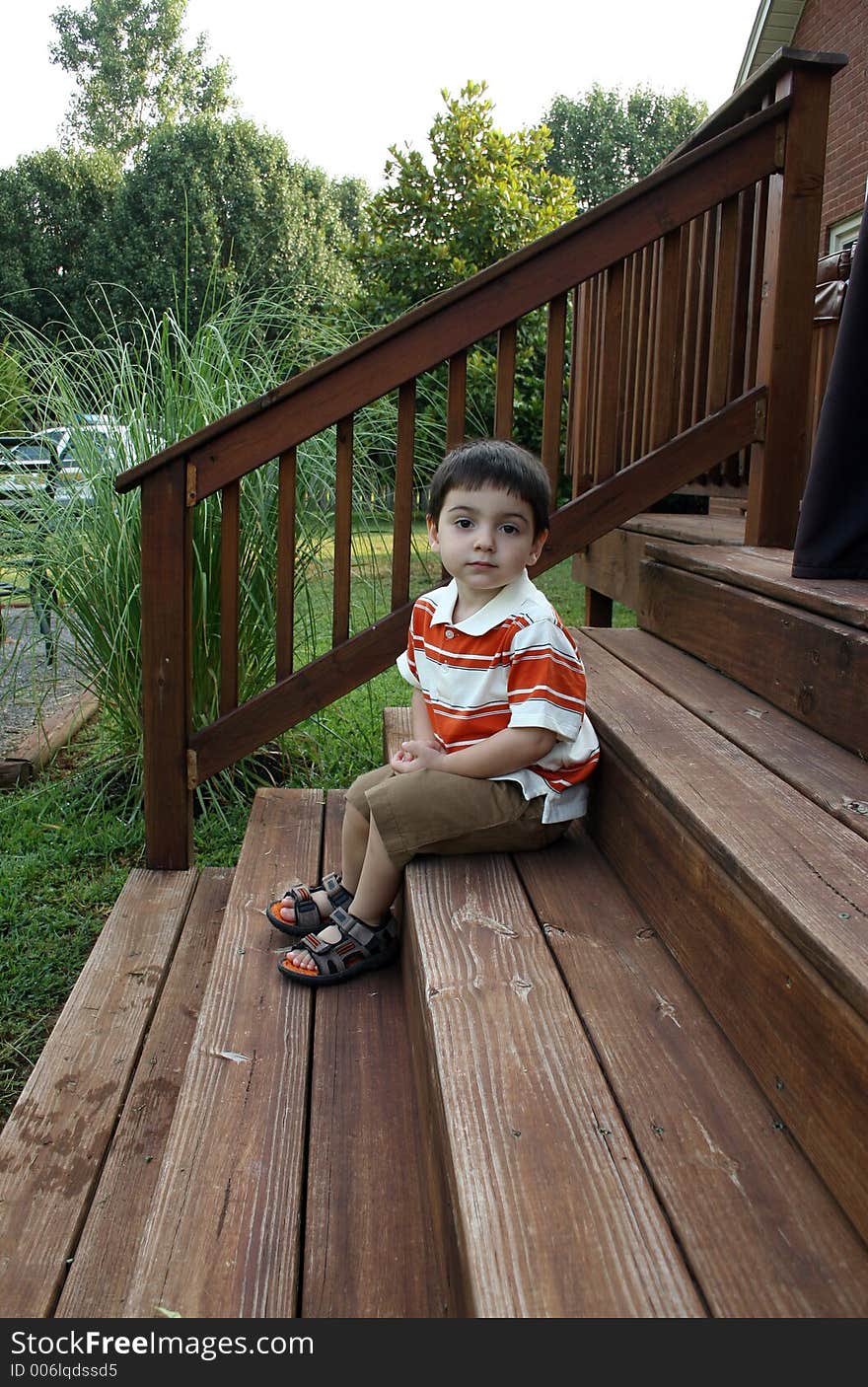 Toddler boy sitting on deck steps.