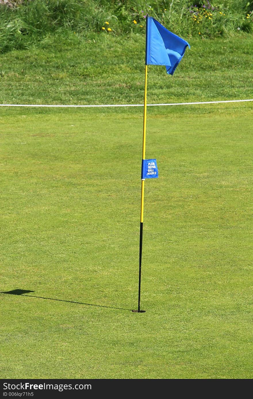 A blue golf flag in a the hole on the green on a golfcourse. A blue golf flag in a the hole on the green on a golfcourse