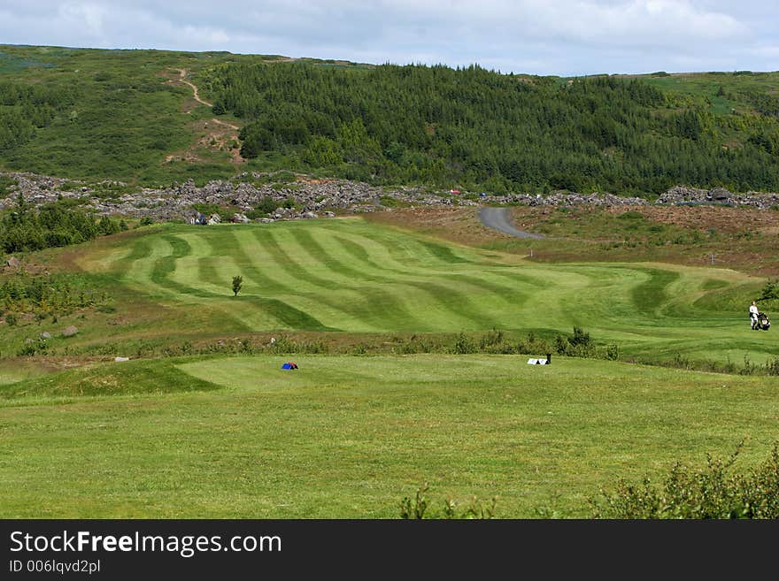 A green golfcourse on a sunny day, people on the greens playing golf. A green golfcourse on a sunny day, people on the greens playing golf