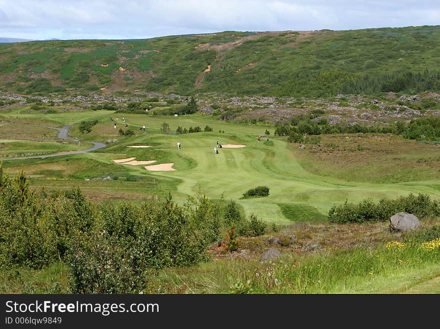 A green golfcourse on a overcast day, people on the greens playing golf. A green golfcourse on a overcast day, people on the greens playing golf