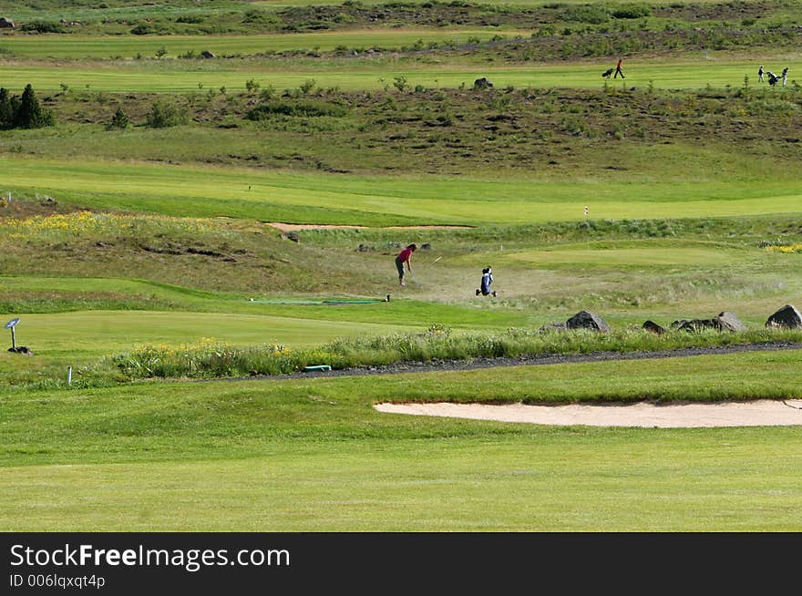 A green golfcourse on a overcast day, people on the greens playing golf