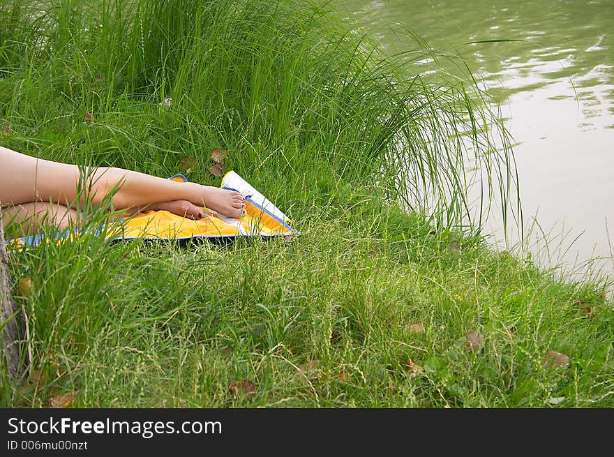 Legs of a tanning girl laying in the grass on the bank of a lake