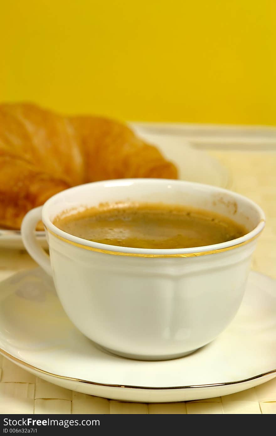 A cup of coffee with croissant in the background. A cup of coffee with croissant in the background