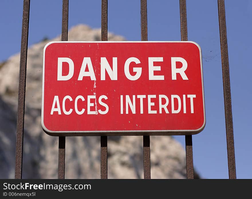 Locked gate with danger sign in french and cliffs in background