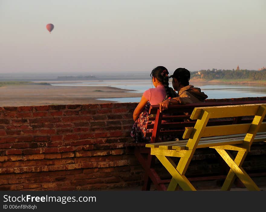 Couple siting in a bench watching the sunset with a ballon in the sky, city of Bagan, Myanmar (Burma)