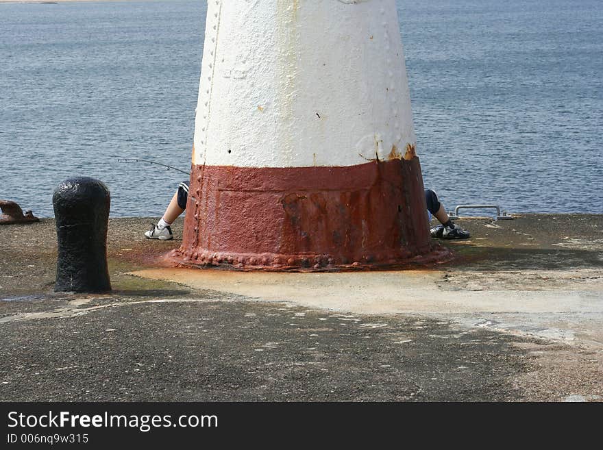 The legs of two boys fishing at the base of a small lighthouse at Cullen Bay, Scotland. The legs of two boys fishing at the base of a small lighthouse at Cullen Bay, Scotland.