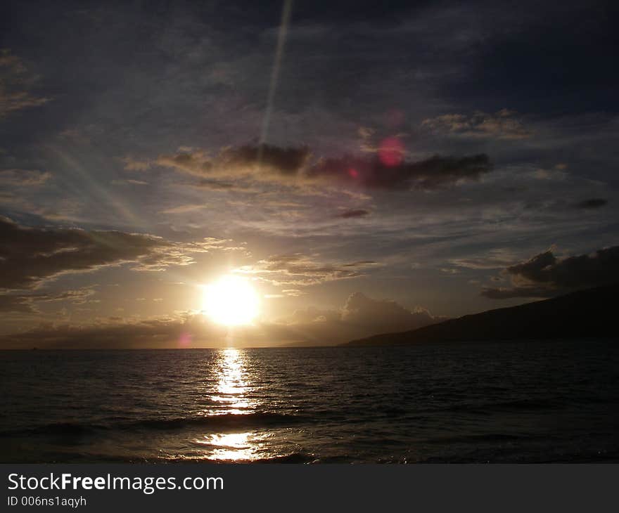 Ocean sunset or sunrise with lens flair and rays, partly cloudy. Hawaii islands off to the side