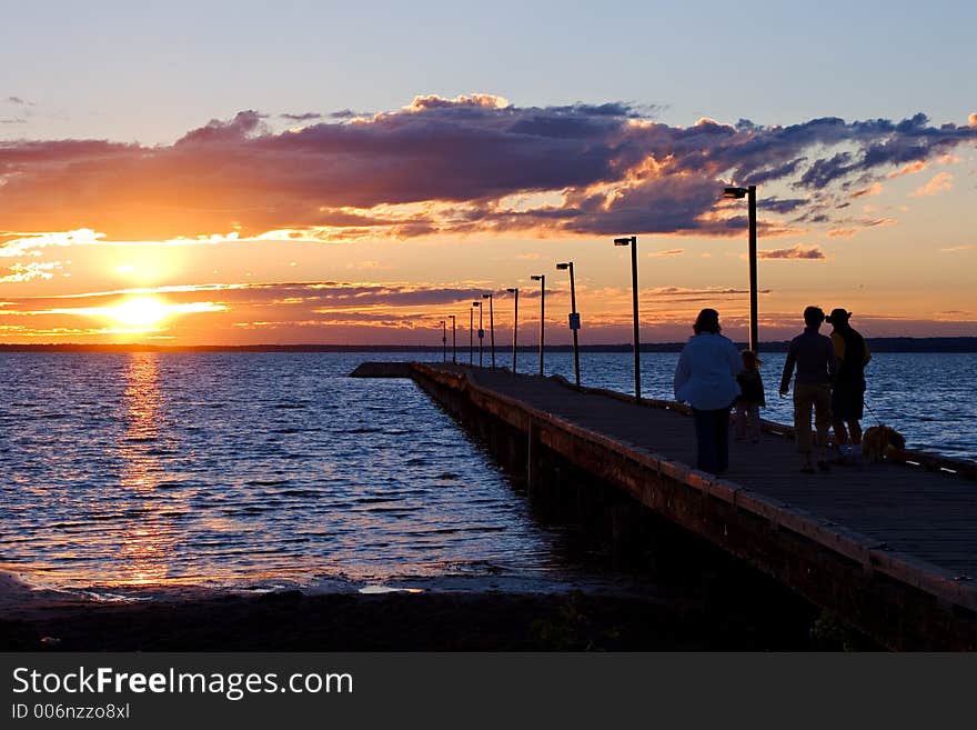 Various people enjoy a walk along a pier at sunset. Various people enjoy a walk along a pier at sunset.