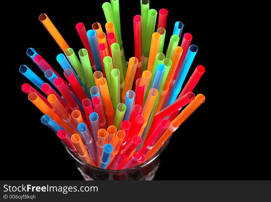 Close-up of vibrant colored straws in clear glass on black background. Close-up of vibrant colored straws in clear glass on black background