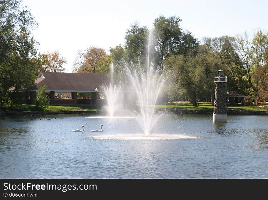 Two fountains and lighthouse in park pond on breezy day. Two fountains and lighthouse in park pond on breezy day.