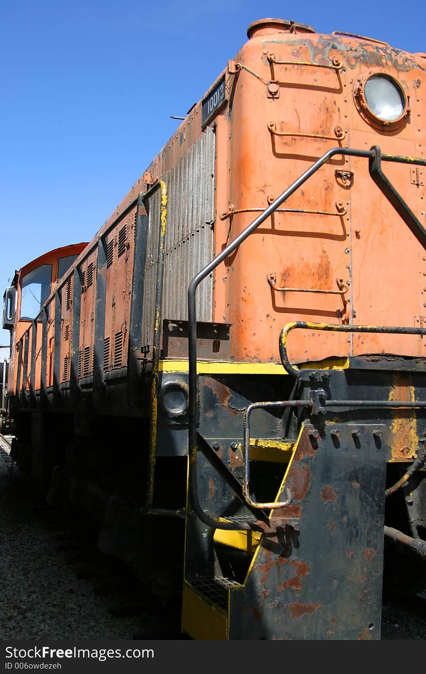 Old weathered orange train engine against a blue sky.