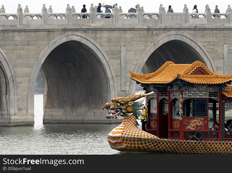 A dragon boat next to an ancient bridge in a scenery park