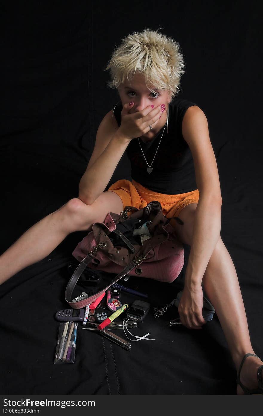 Portrait of beautiful young sexy woman on black background - looking at her purse mess