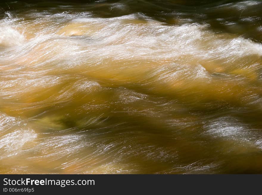 Hues of green and gold along with light trails from the reflection of the sun in flowing water. Hues of green and gold along with light trails from the reflection of the sun in flowing water