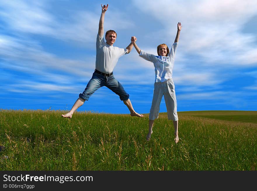 Jumping couple in field under clouds