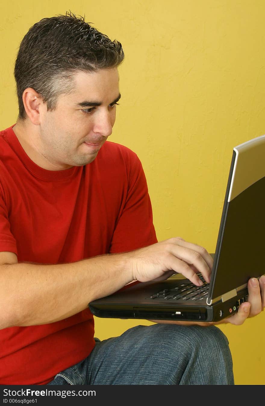 Thirty-two year old man with laptop against yellow wall.