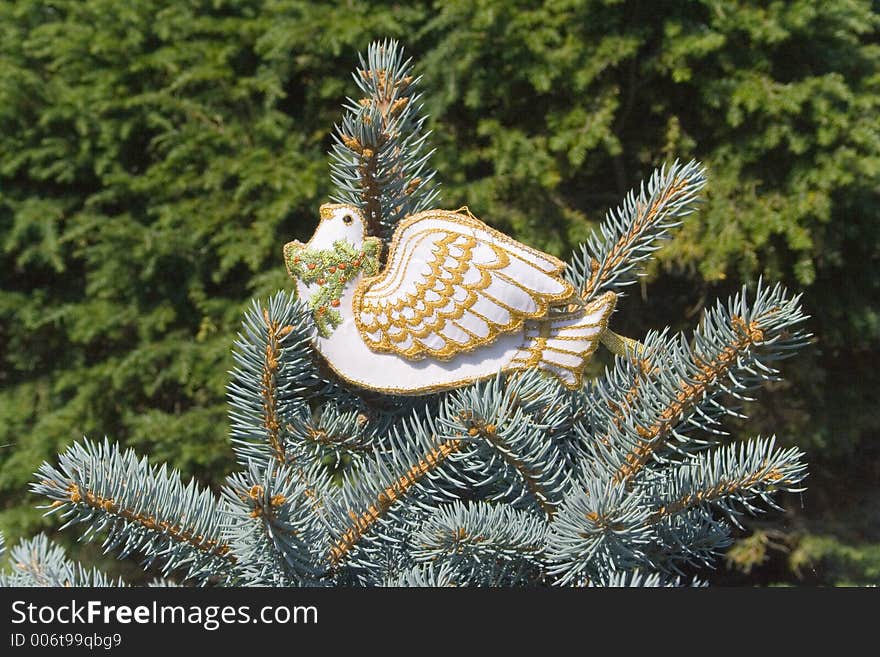 The Dove of Peace rests atop the uppermost branches of a christmas tree. Beautifully embroidered with gold thread, a wreath of holly with red berries adorns it's neck. The Dove of Peace rests atop the uppermost branches of a christmas tree. Beautifully embroidered with gold thread, a wreath of holly with red berries adorns it's neck.