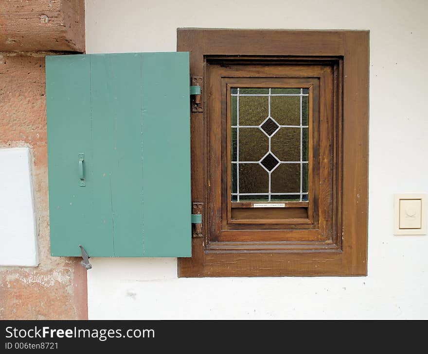 A wooden window frame with a green wooden shutter. The glass of the window is coloured and forms a grid with rhombic inner parts. A wooden window frame with a green wooden shutter. The glass of the window is coloured and forms a grid with rhombic inner parts.