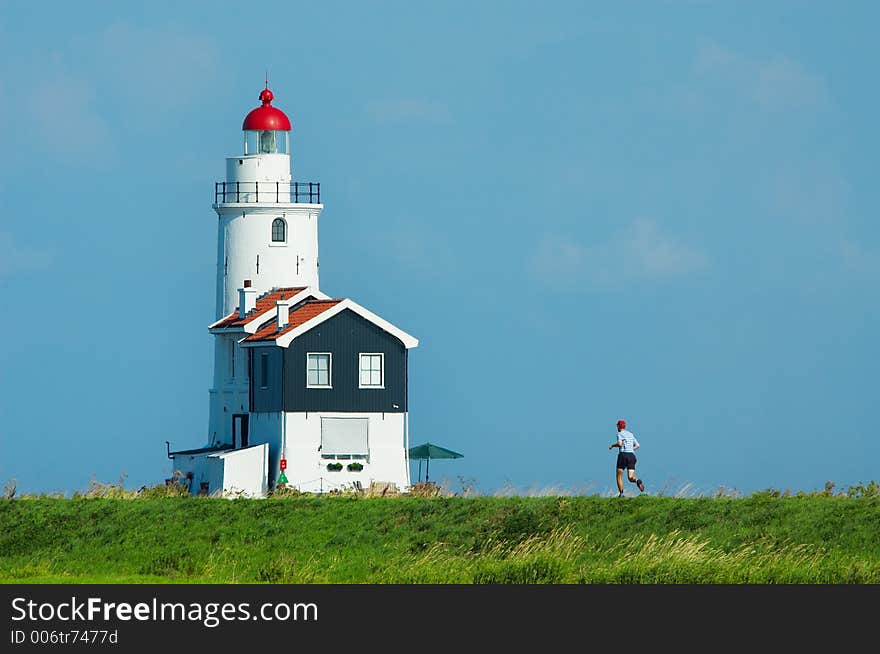 A man jogging towards a lighthouse in summer. A man jogging towards a lighthouse in summer