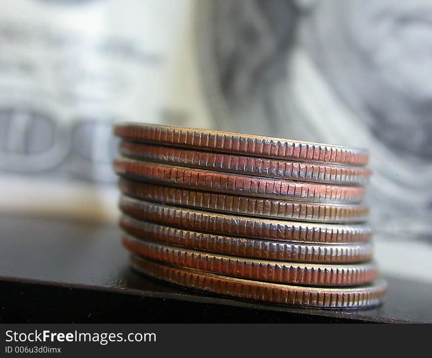 American Quarters stacked in the foreground with an American One Hundred Dollar Bill in the background. American Quarters stacked in the foreground with an American One Hundred Dollar Bill in the background