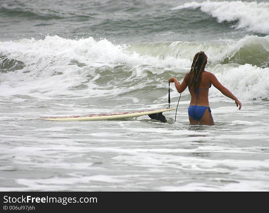 Young girl walking into the ocean dragging a surfboard. Young girl walking into the ocean dragging a surfboard