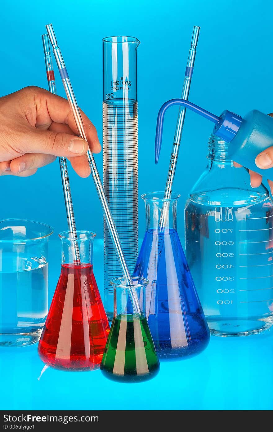 Many different coloured chemical solutions in laboratory glasses with pipettes and two hands on blue background. Many different coloured chemical solutions in laboratory glasses with pipettes and two hands on blue background